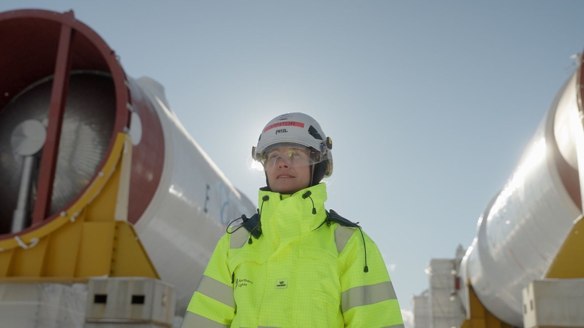 Berry in neon yellow work jacket outside with large machines on either side of her